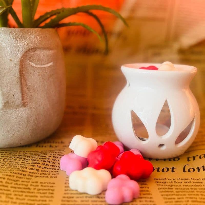 Wax melts în formă de norișori colorați, lângă un suport alb de aromaterapie din ceramică